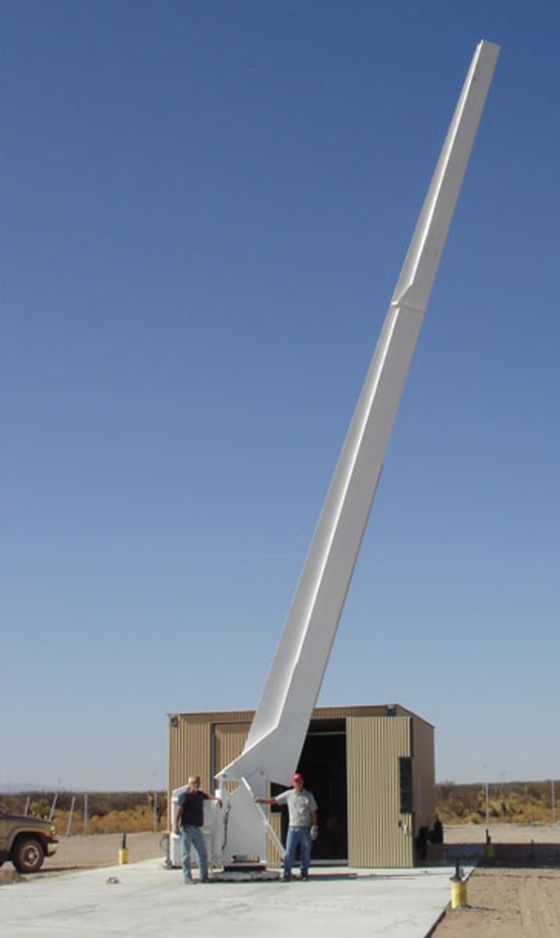 UP Aerospace's launch rail has been raised for the first time at the New Mexico spaceport. In the background, workers are readying the mobile Vehicle Assembly Building that will roll over the launch rail hardware.