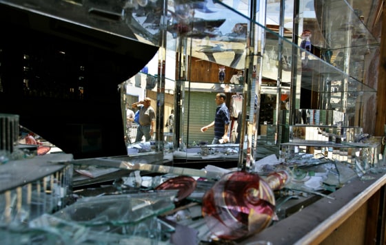 People pass a destroyed shop window on Wednesday in Dahab, Egypt, at the site where one of three bombs ripped through Egypt's Red Sea resort. 