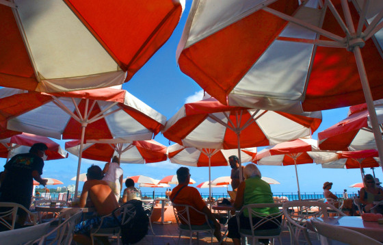 Colorful umbrellas block out the sun for visitors to the beachside Mai Tai Bar at the popular Royal Hawaiian Hotel on Waikiki Beach in Honolulu, Hawaii.