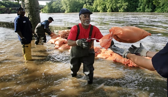 As water rises above the banks of the Schuylkill River, Philadelphia Water Department workers remove submerged sandbags to reuse and protect a firehouse and nearby homes.
