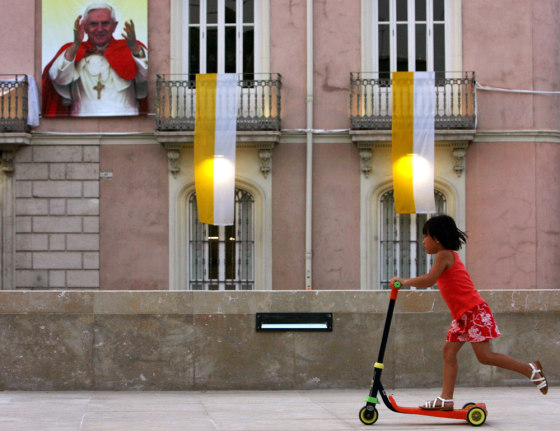 A girl rides a scooter in front of a poster of Pope Benedict XVI in Valencia