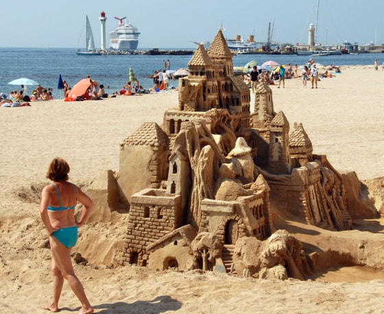 A woman looks at a sand sculpture of a medieval castle Tuesday, July 4, 2006, on a beach in Cannes, France.