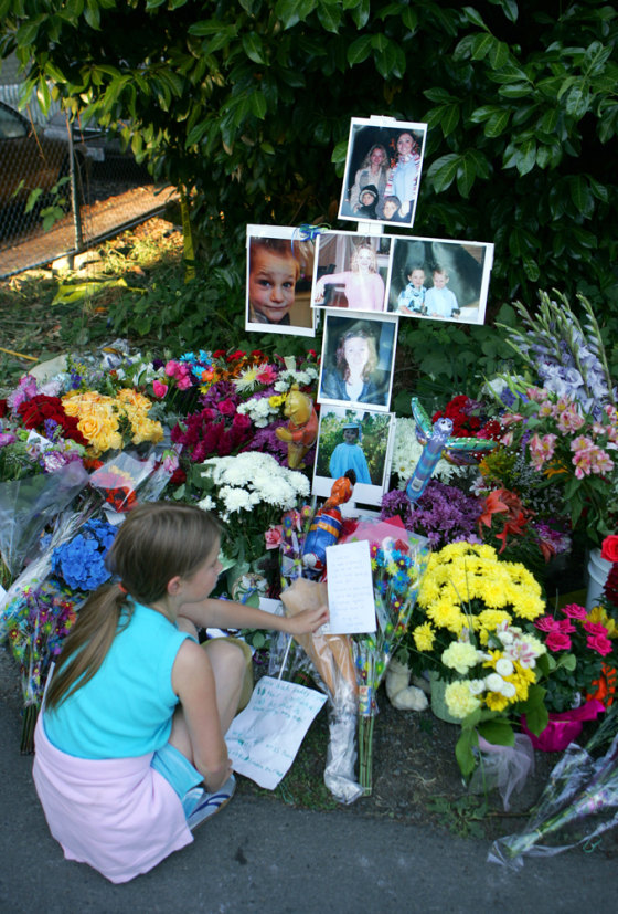 Alina Suyurov sits at the makeshift memorial for four people killed in a house fire in Kirkland, Wash., on Wednesday. All four people found dead in a home fire Monday were stabbed in the neck before the blaze was set, police say.