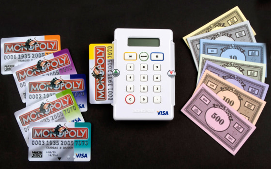 This photo provided Hasbro shows a British version of the classic Monopoly board game which abandons traditional paper money, right, for an electronic debit card system. It's not clear if the system charges a transaction fee.