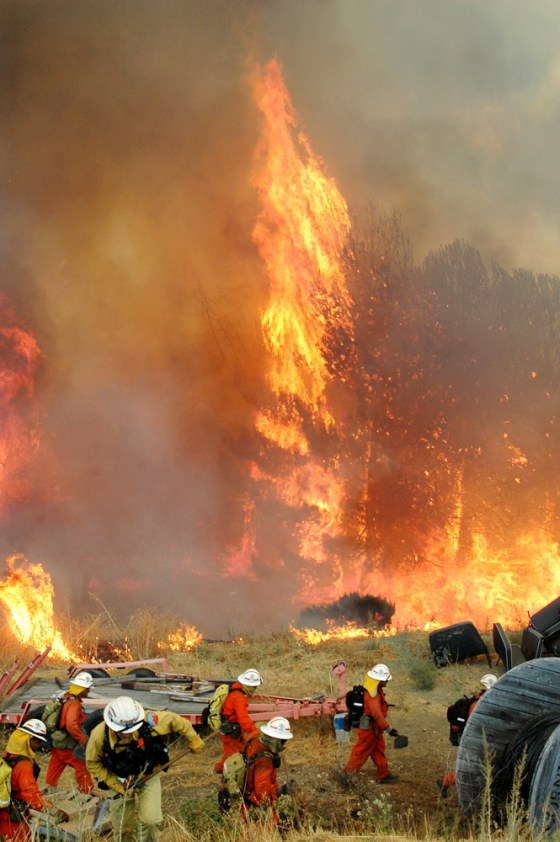 A Los Angeles County fire crew moves out of the area Monday as flames tear through trees in a semi-rural area north of the city. The fire, burning towards the Angeles National Forest, is one of several dozen burning across the West.