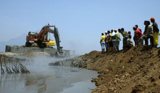Residents look at an excavator at a site flooded by hot mud leaking from an oil and gas exploration in Sidoarjo