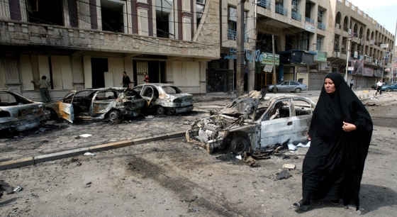 An Iraqi woman walks past burned cars an