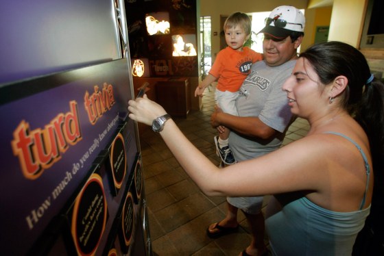 Stephanie Rey, right, tests her skill at "turd trivia" as she, her father, Gustavo Rey, and her son, Phillippe Mann, tour an exhibit on excrement titled "The Scoop on Poop" at Miami Metrozoo in Miami.