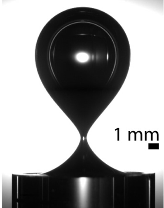 An air bubble is on the verge of pinching itself off from the end of a cylindrical glass nozzle submerged in water. The scale bar indicates 1 millimeter, or about 0.04 inch.