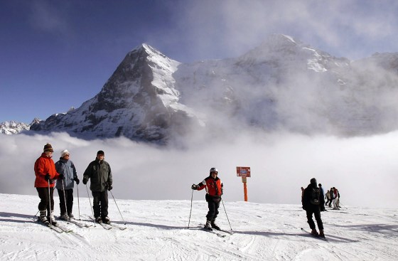 Ski tourists enjoy the sun on top of the Lauberhorn mountain, backdropped by the Eiger, left, and Moench mountains in Wengen, Switzerland.