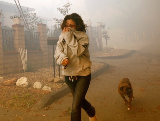 Wendy Gonzalez rushes with her dog from her family's home on Sunday as a wildfire draws near in Moorpark, Calif. A fire driven by strong Santa Ana winds threatened hundreds of homes.