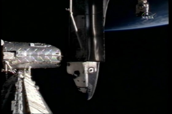 The space shuttle Discovery is docked to the shiny Destiny laboratory module on the international space station on Monday, as seen from a vantage point elsewhere on the station. The left wing is facing the camera. A sliver of sunlit Earth is visible at upper right.