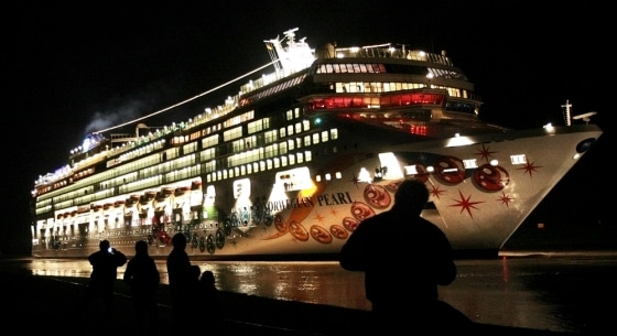 People stand on a dyke watching cruise ship Norwegian Pearl on its passage from Papenburg to the North Sea