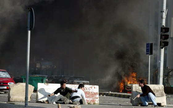 Lebanese youths take cover as a car burn