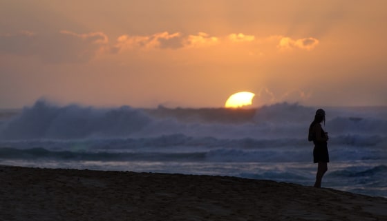 A women watches the sun set behind swellls of waves rolling to the shore at Sunset Beach on the north shore of Oahu.