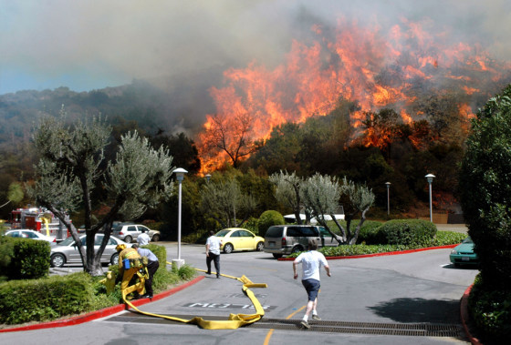 Residents run for their cars in a parking lot behind the Oakwood Apartments as a wildfire burns in the Hollywood Hills section of Los Angeles on Friday.