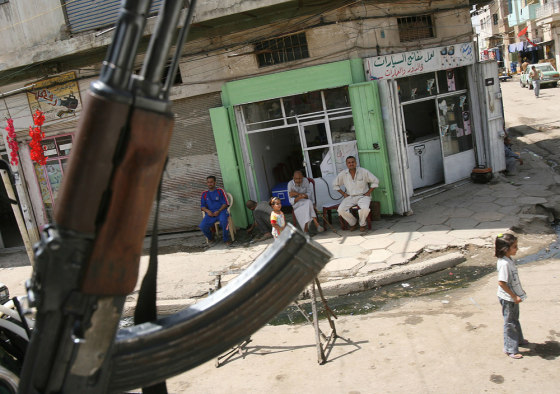 People sit outside a shop as an Iraqi army officer patrols in central Baghdad, on Monday.