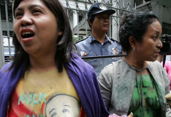A riot police officer watches from the back as Filipino mothers bare their breasts to reveal colorful slogans during a protest outside the Supreme Court Tuesday, June 19, 2007 in Manila, Philippines, to coincide with the highest court's session on the milk code.