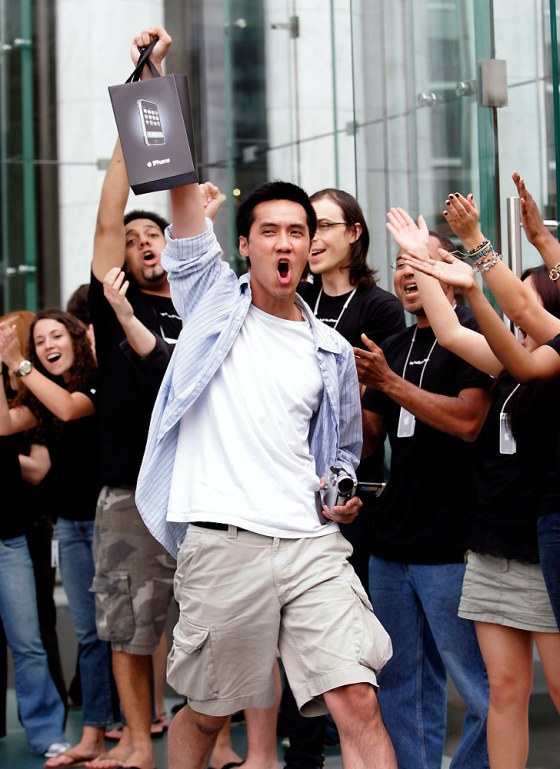 Surrounded by cheering Apple Store employees, one of the first iPhone buyers leaves the store on Fifth Avenue in New York