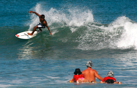 Foreign tourists watch a local surfer at a beach in Kuta