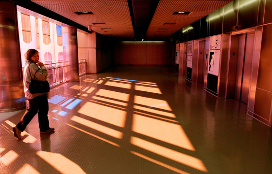 A woman walks through a Terminal A parking garage access corridor bathed in streams of red and yellow light at Logan International Airport in Boston. The colored light was generated by tinted window panes created by Christopher Janney as part of his interactive public art project at the airport.