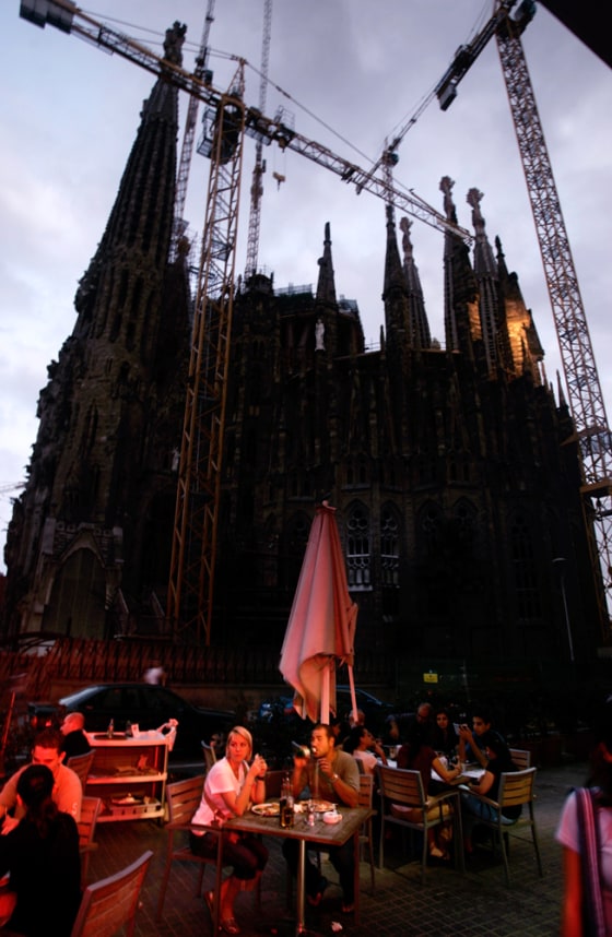 Tourists have dinner Tuesday in front of the Sagrada Familia cathedral, seen without its usual illuminations in Barcelona.