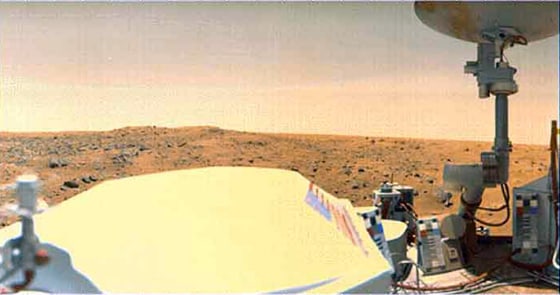 A Viking 1 Lander image of Mars' Chryse Planitia. The large white object at lower left and center, with the American flag on the side, is the spacecraft's radiothermal generator (RTG) cover.