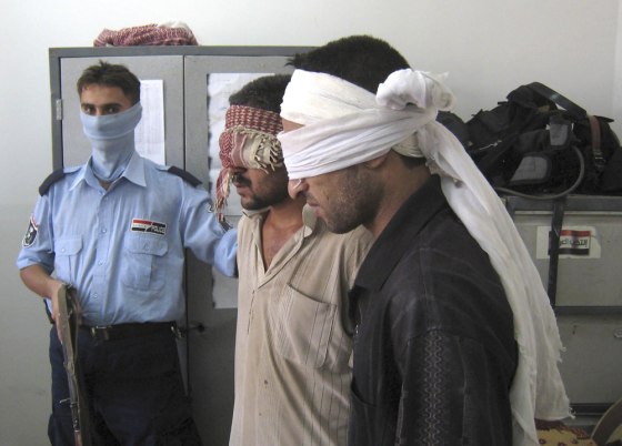 An Iraqi police officer guards two detainees who were arrested as they tried to launch a Katusha rocket at the Kirkuk airport, north of Baghdad, on Sunday.