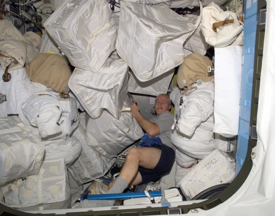 Astronaut John Phillips seems nearly buried as he stows storage bags in an air lock on the international space station. Trash and other items are piling up aboard the station, waiting for their return to earth aboard the shuttle Discovery.