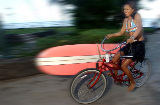 SURFER BIKES WITH HER SURF BOARD