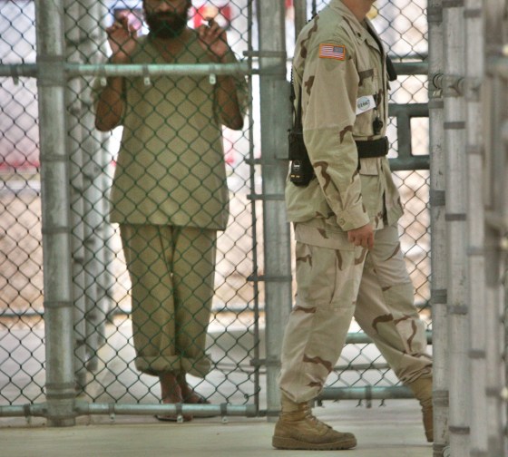 In this photo, reviewed by US military officials, a detainee at the Camp 5 maximum security prison at Guantanamo Bay holds onto a fence as a U.S. military guard walks past.