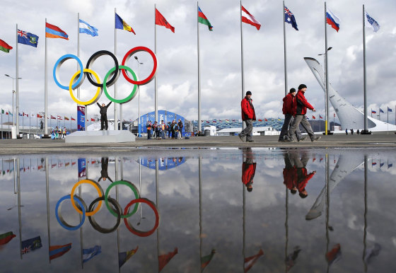 Image: People walk past the Olympic rings and the cauldron for the Olympic flame as preparations continue for the Sochi 2014 Winter Olympics.