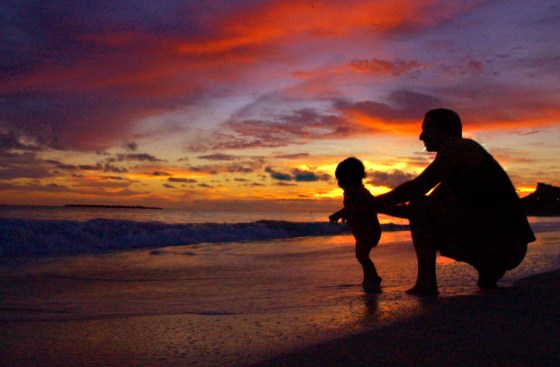 Image: A man plays with his son on the beach at sunrise.