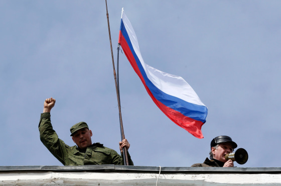 Image: A man holds a Russian flag on the roof of the naval headquarters in Sevastopol