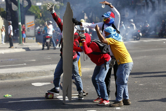 Image: Anti-government protesters take cover from the police behind makeshift shields in Caracas