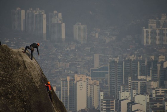 Image: Climbers scale a rock face as a think layer of pollution hangs over the Seoul skyline