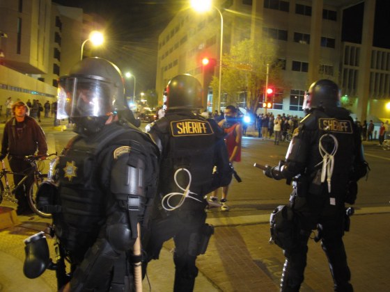 Riot police stand guard in front of protesters in downtown Albuquerque, N.M., Sunday, March 30,2014. Hundreds of protesters marched past riot police in Albuquerque on Sunday, days after a YouTube video emerged threatening retaliation for a recent deadly police shooting. The video, which bore the logo of the computer hacking collective Anonymous, warned of a cyberattack on city websites and called for the protest march. (AP Photo/Russell Contreras)