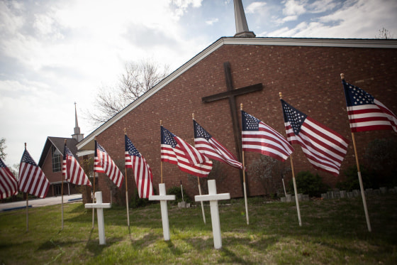 Image: A memorial of three white crosses and 16 flags stands at the Central Christian Church