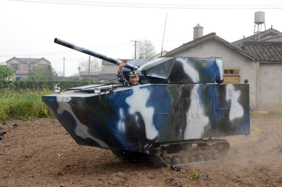 Image: Jian lin waves in his home-made replica of a tank during a trial run, at a village in Mianzhu