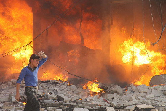 Image: A man walks past a burning building following a reported air strike by pro-regime forces on the northern Syrian city of Aleppo