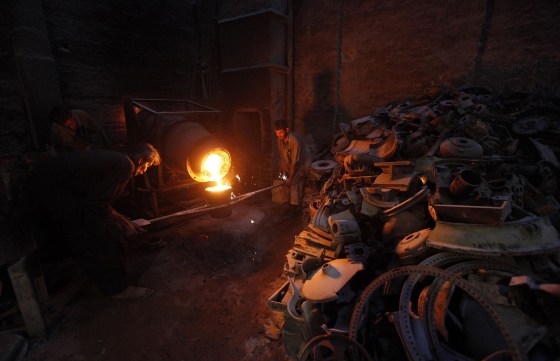Image: Labourers fill a pot with melted iron to pour into a casting mould to make machine parts in a foundry in Karach