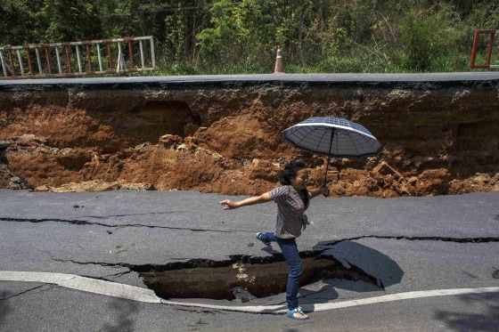 Image: A woman with an umbrella jumps over a hole on a highway road, damaged by Monday's earthquake in Chiang Rai, in northern Thailand
