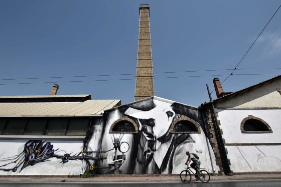 Image: A man rides by a new mural by INO at the Athens Technopolis, an industrial museum and a major cultural venue
