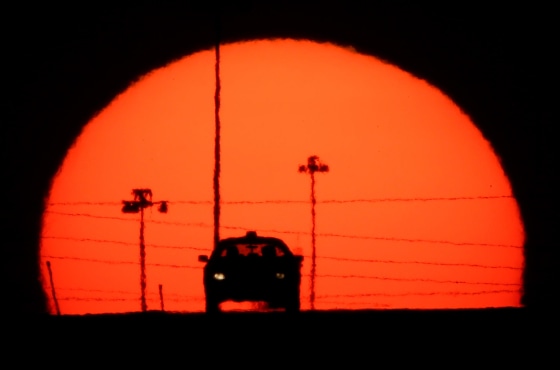 Image: A car is silhouetted against the setting sun