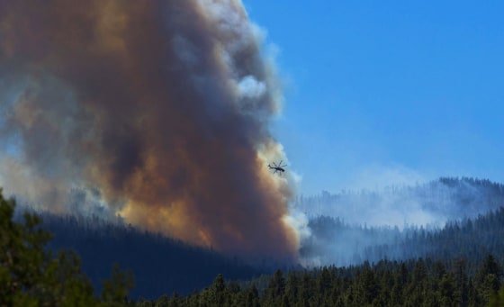 A helicopter battles the blaze with lake water as smoke rises from the trees of the San Juan fire near Vernon, Az., on June 27. Authorities say communities mostly populated with summer homes are under mandatory evacuation orders as of Thursday evening due to the growing wildfire.