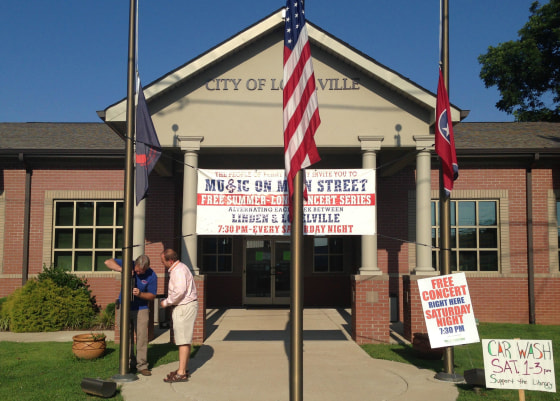 Image: Lobelville Mayor Robby J. Moore, right, and business owner Robert Mathis lower flags in front of City Hall in Lobelville, Tenn.