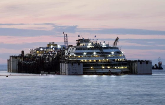 The ill-fated Costa Concordia cruise liner is illuminated by its own on-board lighting system at dawn on July 15 on the second day of the re-floating operation off the island of Giglio.
