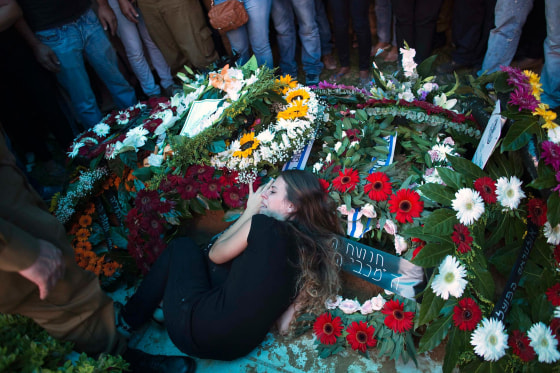 Image: The girlfriend of Israeli soldier Yifrah mourns as she lies atop his grave during his funeral near Tel Aviv