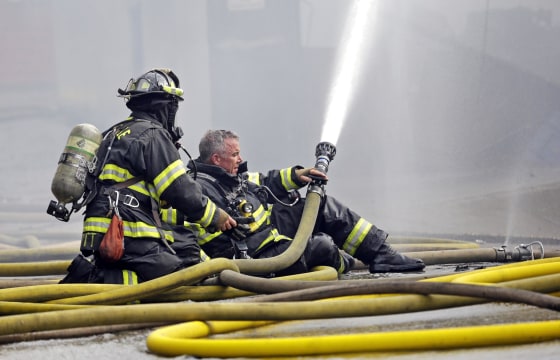 Image: A firefighter briefly goes without his helmet as he prepares to put on a mask while hosing down a building on fire