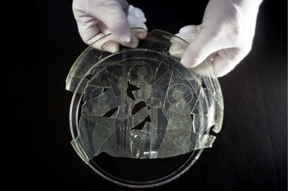 An employee in at the Museum of Archaeology of Linares shows off a glass dish that bears the engraved image of a short-haired Jesus without a beard, flanked by two haloed apostles thought to be Peter and Paul.